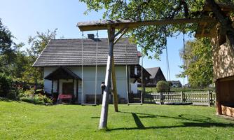 A quiet garden with a swing and a small white house in the background. The grass is green and the sun is shining.