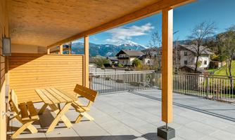 A modern terrace with wooden furniture and a view of the mountains. The surroundings are quiet and inviting.
