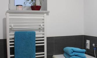 A modern bathroom with a washing machine and a heater. Blue towels and a small plant provide a fresh accent.