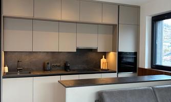 Modern kitchen with elegant gray cabinets and a dark countertop. Next to the kitchen is a cozy gray sofa.