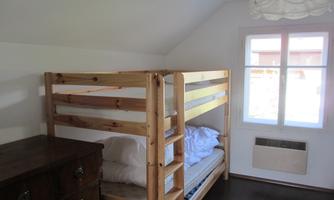 A simple bedroom with a wooden bunk bed. A window provides natural light and a beautiful view.