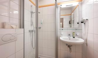 A modern bathroom with a shower and a sink. The walls are tiled with white tiles and there is a large mirror.