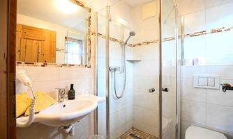 A modern bathroom with a shower and a sink. The walls are light tiled and there are wooden details in the room.