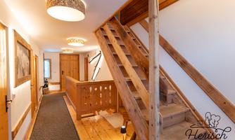 A bright hallway with wooden coverings and a staircase. There are modern lights and an inviting atmosphere.