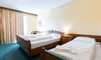 A simple room with two single beds and bright walls. The windows are covered with curtains and there is a nightstand next to each bed.