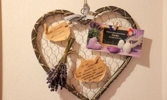 A heart-shaped wall decoration made of wire with dried flowers and handwritten notes. Additionally, a thank you card and small decorative elements are hanging from it.