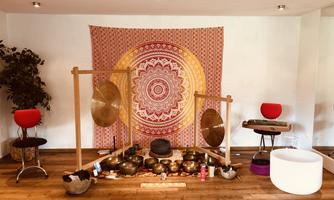 A quiet meditation room with sound bowls and gongs. In the background, there is a decorative tapestry and some seating options.