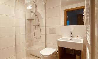 A modern bathroom with a walk-in shower and an elegant sink. The walls are light tiled and the lighting creates a pleasant atmosphere.