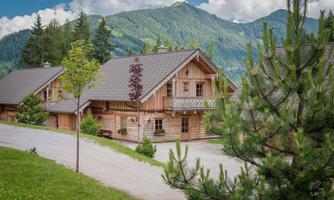 A charming wooden house in a picturesque mountain landscape. The surroundings are green with trees and gentle hills.