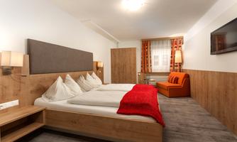 A modern bedroom with a double bed and cozy furnishings. The warm wood tones and the red decorative pillow create an inviting atmosphere.