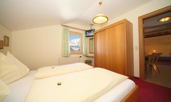 A cozy bedroom with two beds and a wooden wardrobe. A beautiful view of the mountains can be seen through the window.
