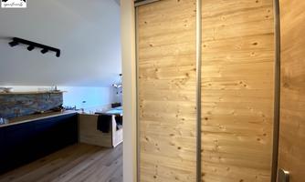 A bright and modern room with a wooden door. In the background, there is a kitchen with an elegant countertop.
