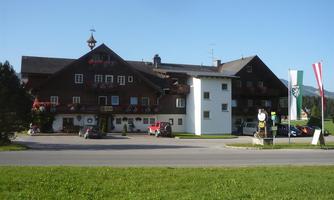 A traditional alpine hotel with a wooden facade and beautiful flower boxes. In the foreground, some cars and flags can be seen.