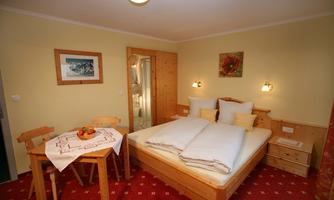 A cozy bedroom with a double bed and wooden furniture. Fresh fruit and a tablecloth are on the table.
