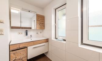 A modern bathroom with wooden accents and a bright, neutral design. Large windows provide plenty of natural light.
