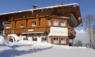 A charming wooden building in alpine style, surrounded by deep snow. Snow-covered mountains are visible in the background.