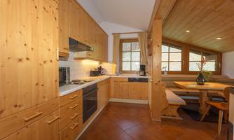 A cozy kitchen with wooden furniture and modern appliances. Large windows provide plenty of daylight and an inviting atmosphere.