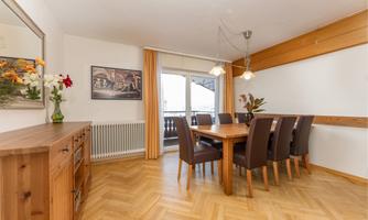 A cozy dining area with a wooden table and chairs. Large windows provide plenty of light and a beautiful view outside.
