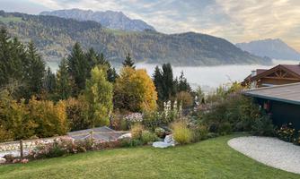 A picturesque landscape with green meadows and colorful trees. In the background, the mountains and a misty valley floor can be seen.