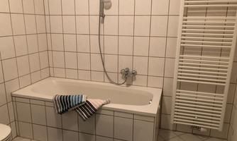 A modern bathroom with a bathtub and a shower. Towels are at the tub and a radiator is on the wall.