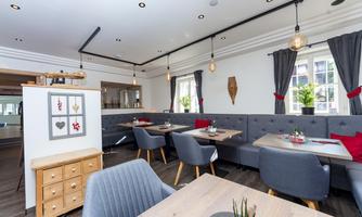 A modern restaurant with cozy seating and stylish decor. Large windows let in plenty of light, and plants create a pleasant atmosphere.