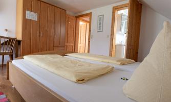 A cozy bedroom with a large bed and two pillows. In the background, wooden cabinets and an open door can be seen.