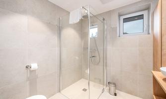 A modern bathroom with a glass shower and bright tiles. Natural light streams in through a window.