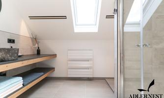 A modern bathroom with skylights and bright tiles. There is a wooden shelf with towels and a glass shower unit.