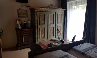A cozy room with two beds and a traditional, colorful wardrobe. A table with a lamp and a bottle of water complements the furnishings.