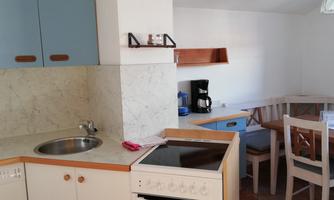 A modern kitchen with blue cabinets and a light wooden countertop. In the background, there is a dining table with chairs and a coffee machine.