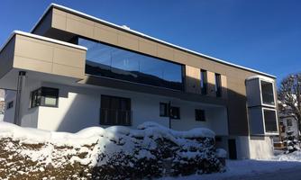 A modern house with large windows and a simple design. Surrounded by snow and under a clear blue sky.