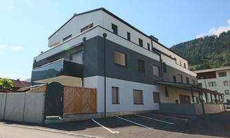 A modern building in a quiet residential area. It has a bright facade and an surrounding parking area.