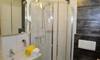 A modern bathroom with a glass shower and a sink. On the sink lie two towels, one yellow and one white.