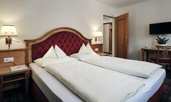 A cozy hotel room with two single beds and a rustic wooden design. The walls are light, and there is pleasant lighting as well as a small desk.