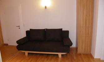 A simple living room with a brown sofa and a wooden shelf. The walls are in light shades and the light creates a warm atmosphere.
