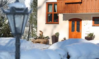 A charming house with an orange door and windows.  
Surrounded by snowy ground and a lantern-lit path.