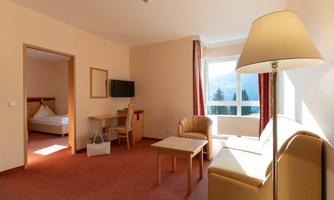 A cozy hotel room with a sofa, a table, and a television. Daylight is shining through the window.