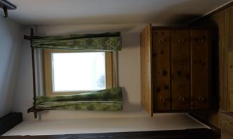 A bright room with a window and green curtains. In front of the window is a wooden-colored dresser.