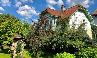 A beautiful house surrounded by lush greenery and flowers. The sky is clear with some clouds.