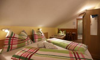 A cozy bedroom with two beds and colorful pillows. The room has a slanted ceiling and is well-lit.