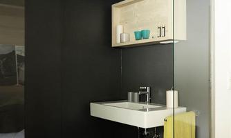 A modern bathroom with a white sink and a glass shower wall. On the wall, there is a shelf with decorative containers and a yellow towel.