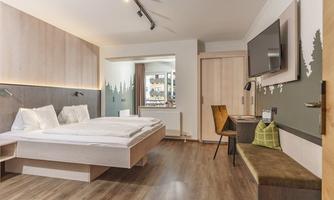 A modern hotel room with a double bed, a desk, and a television. The warm wood tones and minimalist design create a cozy atmosphere.