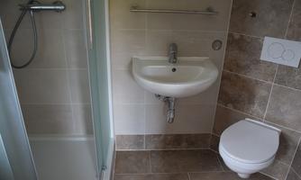 A modern bathroom with a shower, a sink, and a toilet. The walls are tiled with bright, glossy tiles.