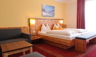 A comfortable hotel room with two single beds and wooden furnishings. The room is bright and friendly, with a cozy seating area and a beautiful wall mural.