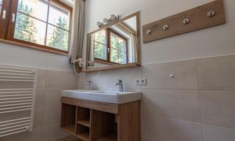A modern bathroom with a wooden vanity and a large mirror. Beams of light come through the window, creating a bright atmosphere.