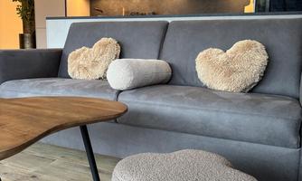 A cozy living room with a gray sofa and heart-shaped cushions. There is also a round ottoman and a wooden table.