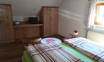A simple bedroom with two beds and wooden wardrobes. A table with chairs and a television is also available.