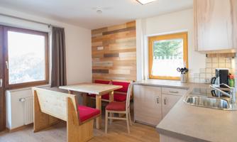 A modern kitchen with a dining table and red chairs. Large windows provide plenty of natural light and a view outside.
