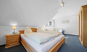 A cozy bedroom with a double bed and wooden furniture. The room has a window and a pleasant atmosphere.