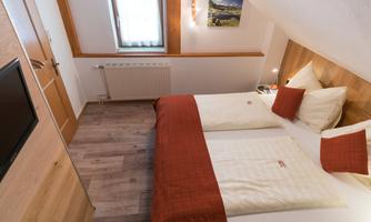 A cozy bedroom with a double bed and wood paneling. The light from a window creates a warm atmosphere.